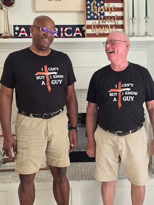 Two men wearing matching t-shirts with a humorous design in a home setting.