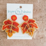 A pair of orange and gold glass beaded earrings shaped like leaves, mounted on card with Inspire Me Fabulous Boutique branding.